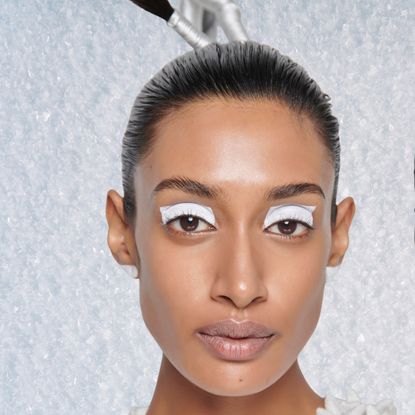 A model with white eye makeup in front of a snowy background. 
