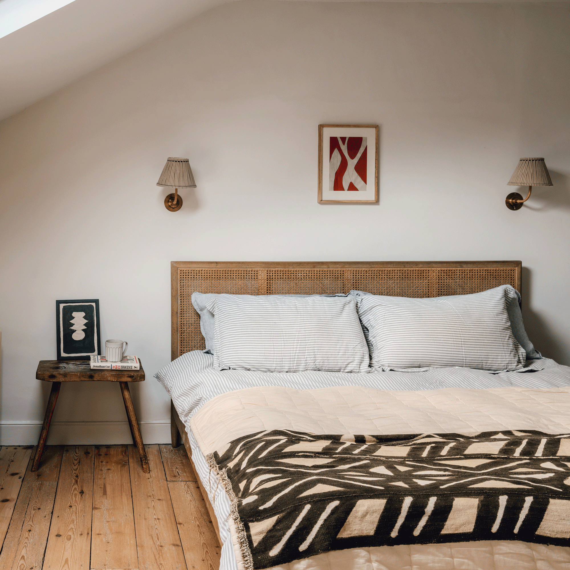 a neutral bedroom with a wicker headboard white bedding and a black and cream patterned throw