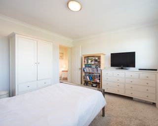 White bedroom with white wardrobe, white bed and black tv on white cabinets