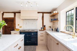shaker kitchen with pink cabinetry and contrasting white island in country kitchen with beams and rustic door