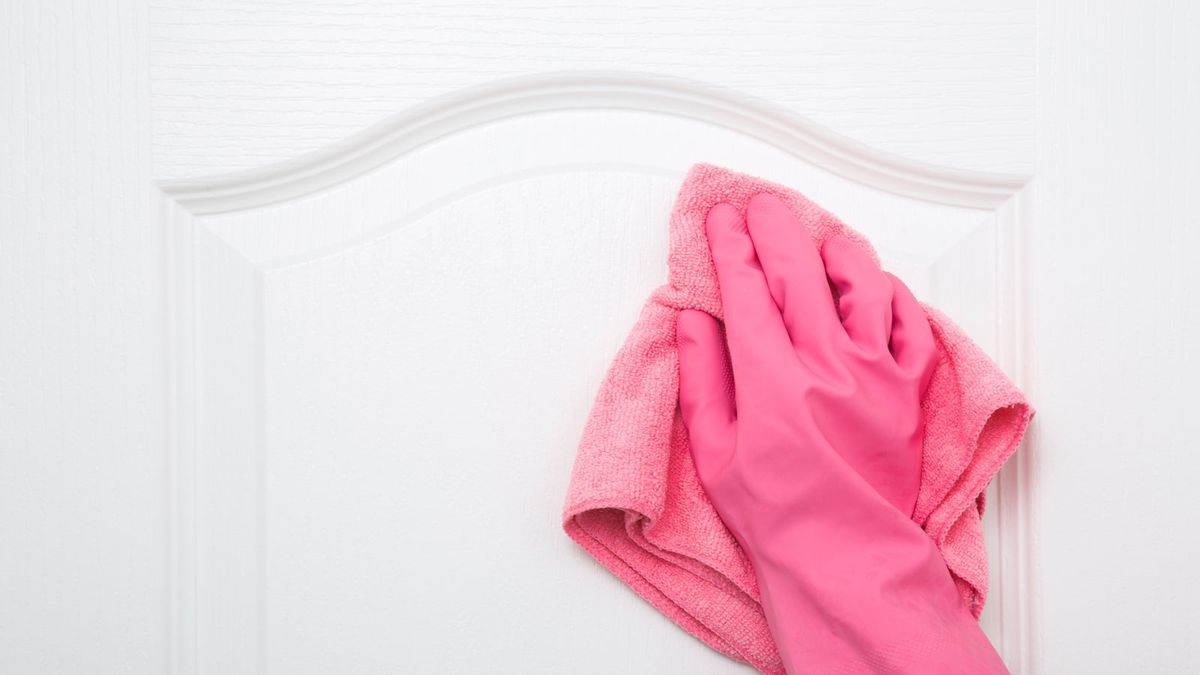 Hand with pink glove and pink cloth wiping down white door