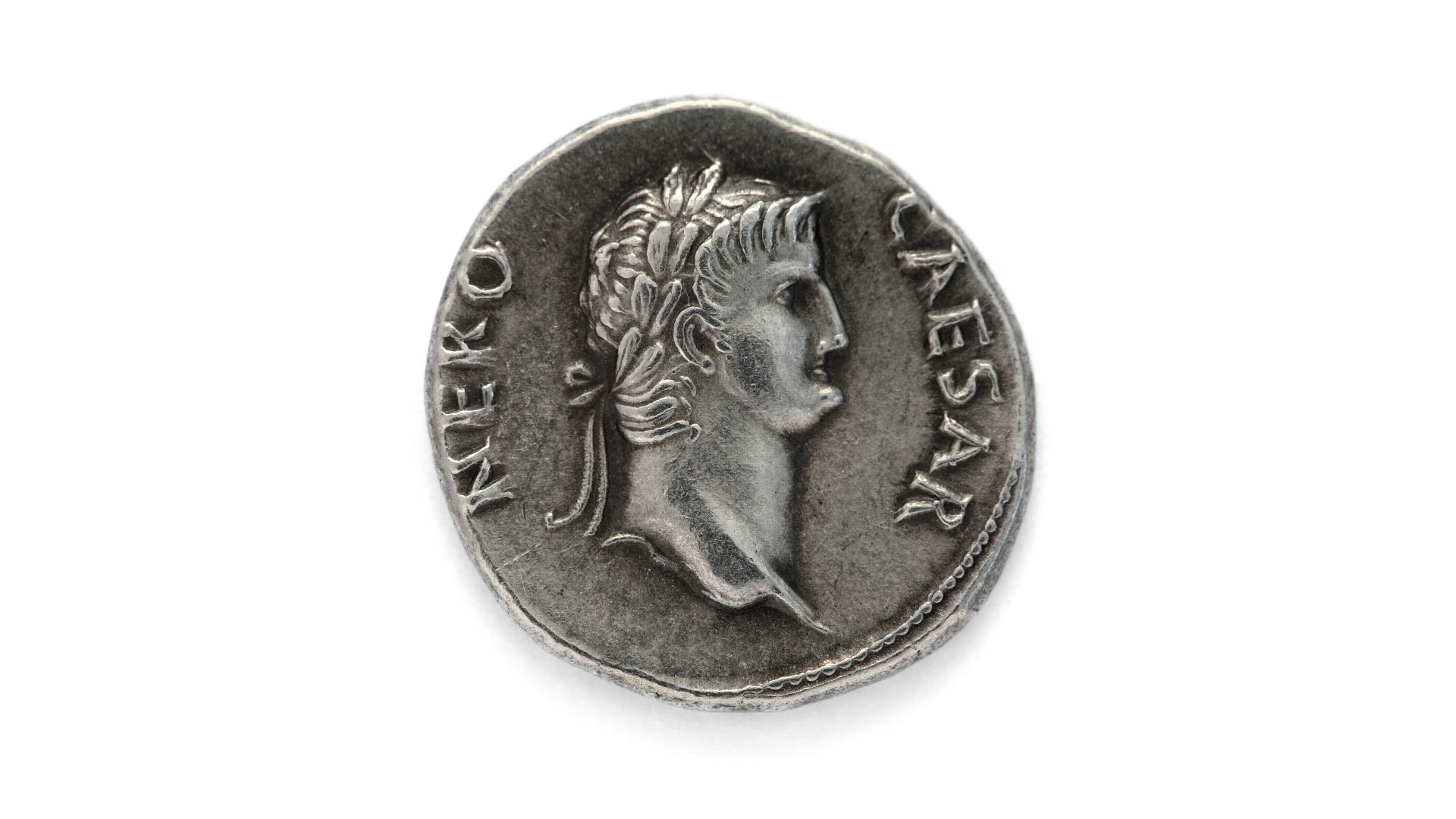 A Roman coin which has the profile of Nero on it. On the left the text reads 'Nero' and on the right it reads ' Caesar.'