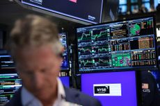 Close-up of a trader on the floor of the New York Stock Exchange (NYSE) with stock charts on a screen in the background