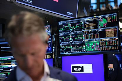 Close-up of a trader on the floor of the New York Stock Exchange (NYSE) with stock charts on a screen in the background