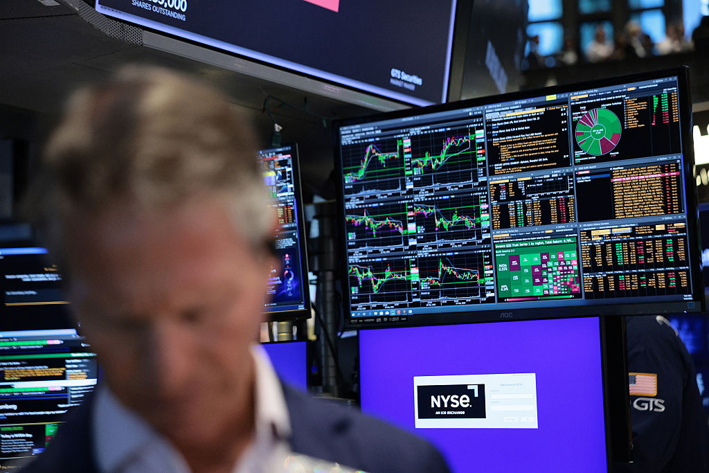 Close-up of a trader on the floor of the New York Stock Exchange (NYSE) with stock charts on a screen in the background