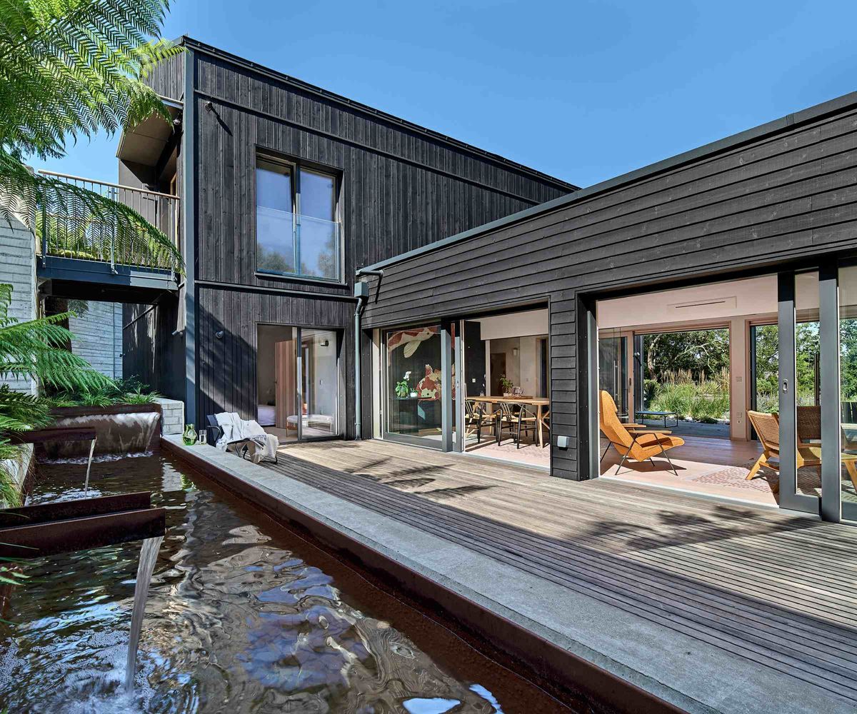 A black timber-clad self build, built by Baufritz, featuring a two-storey and one-storey elements forming a courtyard with Japanese-style water feature