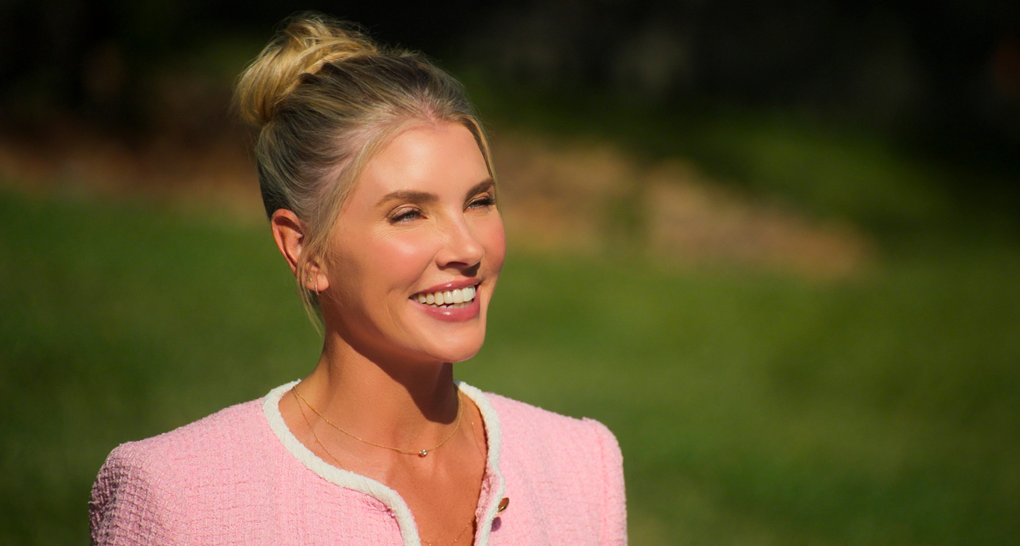 amanda kloots wears a pink suit and her hair in a bun smiling in the netflix reality show let's marry harry