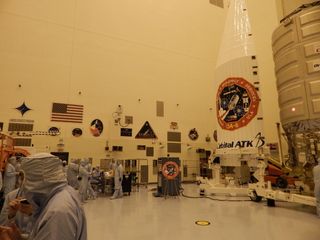 Engineers work to prepare Orbital ATK's Cygnus spacecraft for its March 22 flight; patches from past missions prepared in the Kennedy Space Center clean room are visible on the back wall.