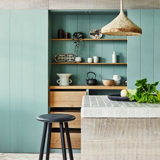 Kitchen with central island, timber clad wall and unit, green and wood cupboards and black stool