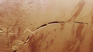 A satellite photo of mars with a massive, curved crack in its surface