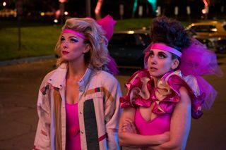 (L to R) Debbie (played by Betty Gilpin) and Ruth (played by Alison Brie) stare into the sky while wearing neon pink outfits in Netflix's GLOW.