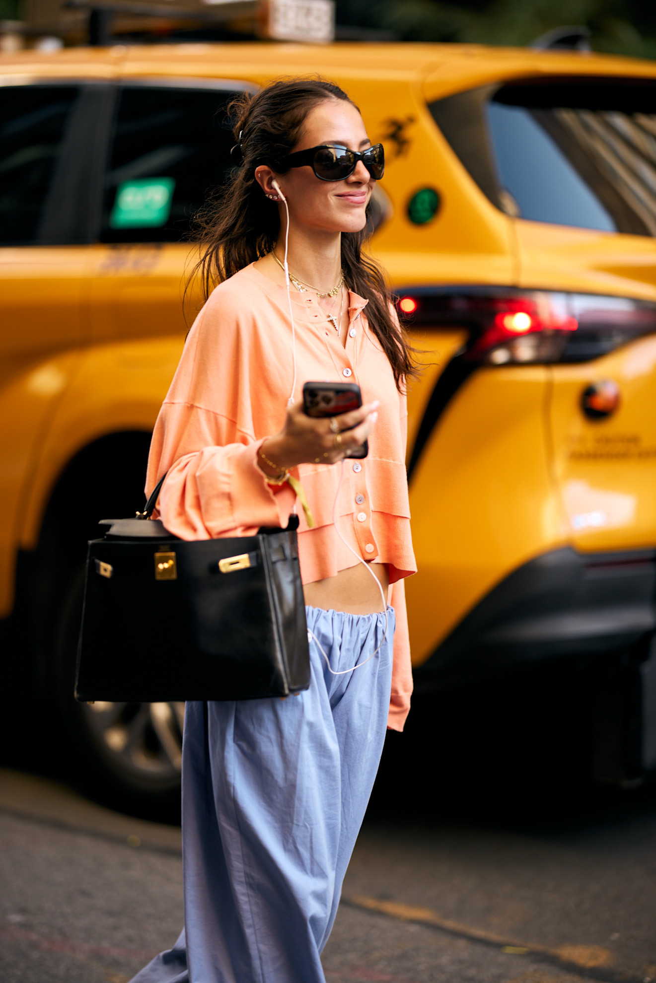 a woman in a pink top and blue pants with sunglasses and a black bag