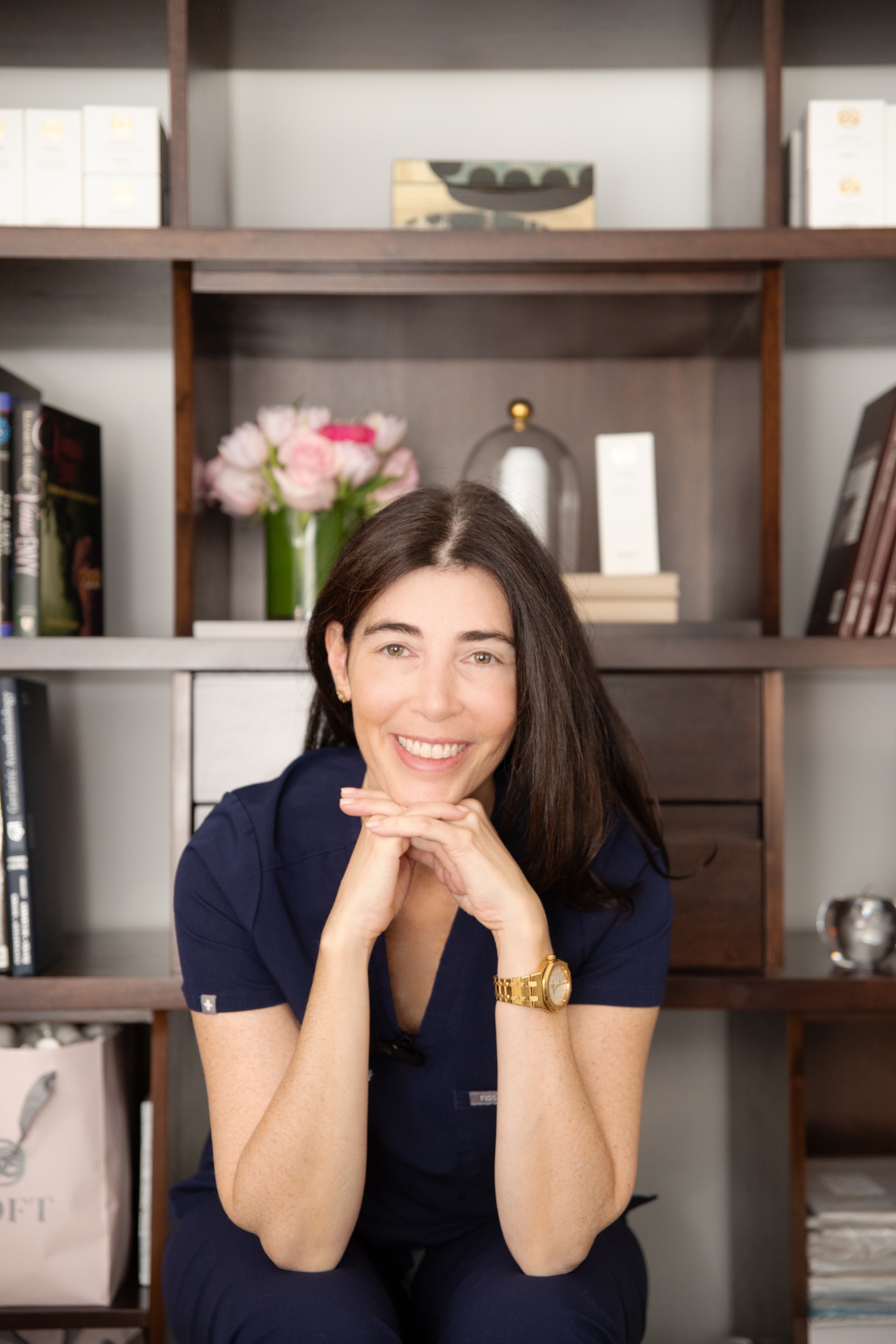 a white woman in blue scrubs with brown hair in front of bookshelves