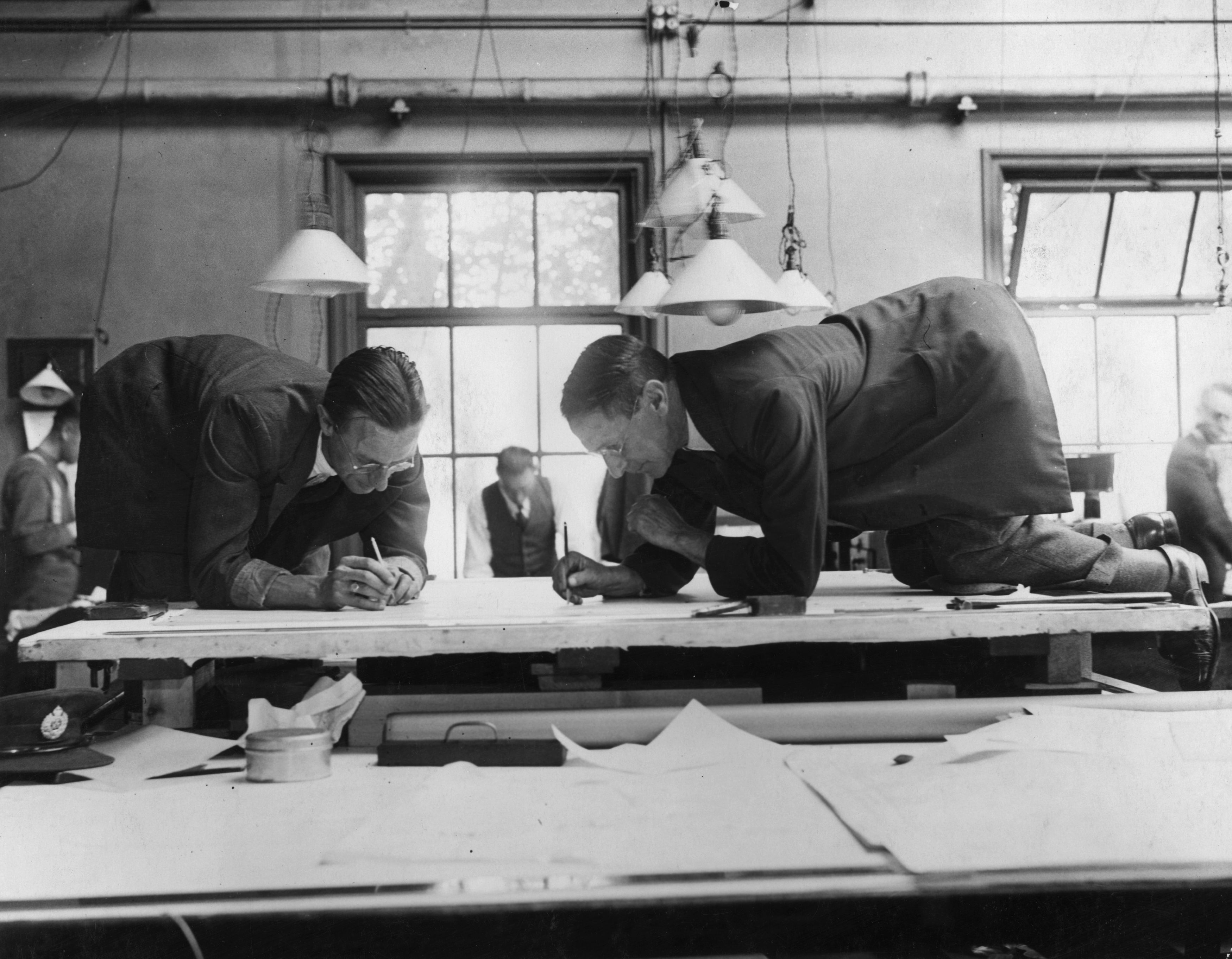 Draughtsmen designing a map at the Ordanance Survey office in Southampton. They're kneeling on a table facing eachother