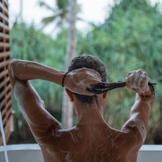 Woman in a bath applying shampoo while looking out at greenery