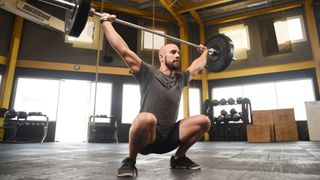 Man performing barbell overhead squat in gym