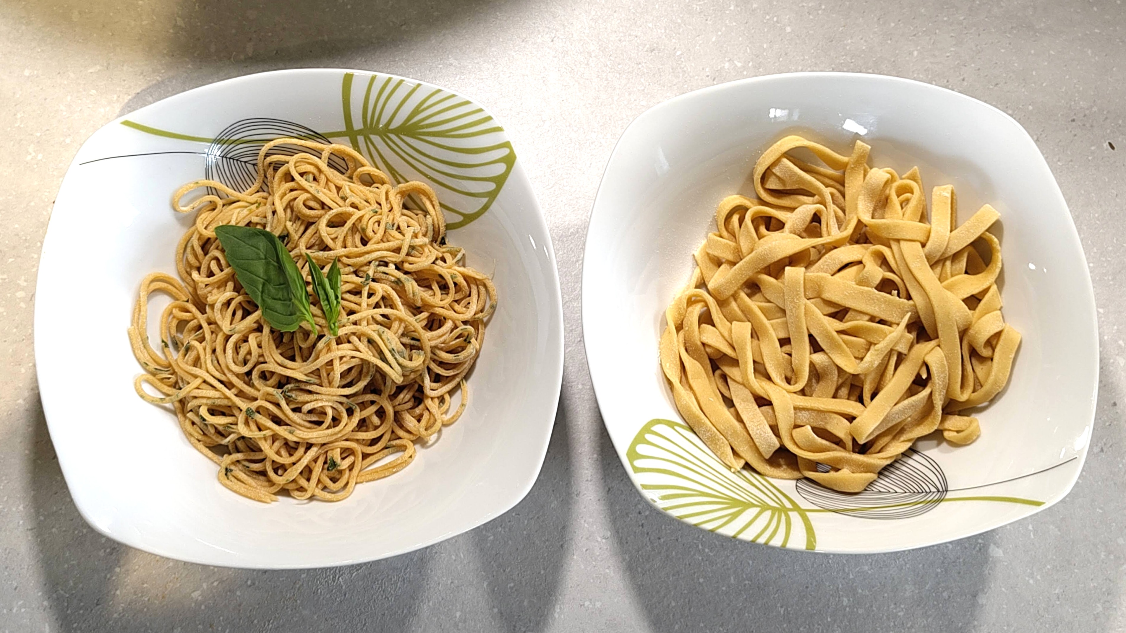Two bowls of freshly made pasta - tomato and basil spaghetti, and egg tagliatelle
