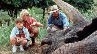 (L to R) Laura Dern as Dr. Ellie Sattler and Sam Neill as Dr. Alan Grant in Jurassic Park, looking at a hurt or dead dinosaur with a young child
