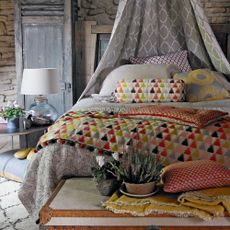 bedroom with brick textured wall and bedding with multi coloured cushions and throw
