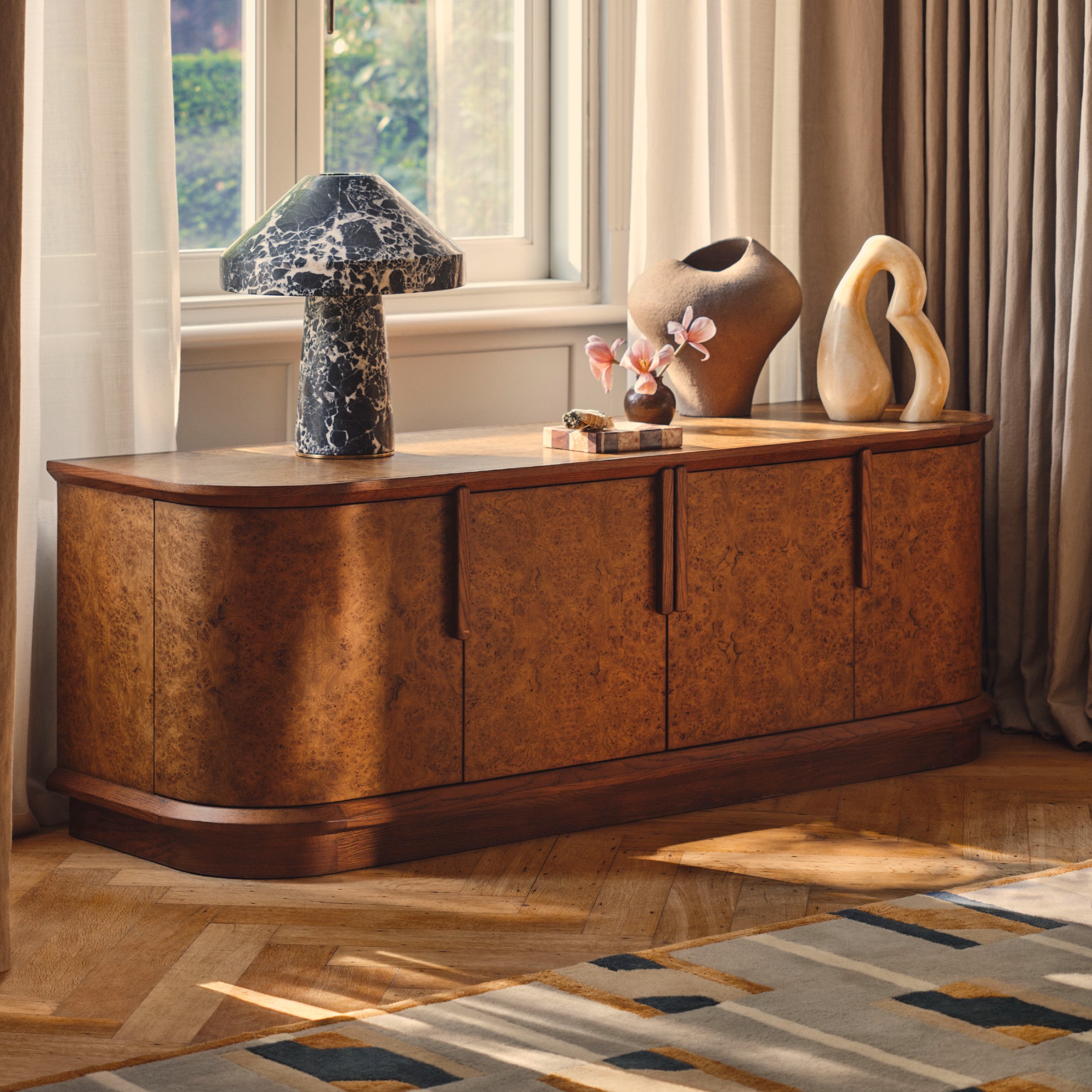 A living room with a Soho Home burl wood-finish sideboard decorated with sculptural objects