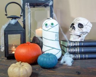 Butternut squash painted in Dulux's warm white and pewter paints with googly eyes to depict a mummy-like character. Pumpkins, skulls, lanterns and cobwebs in background