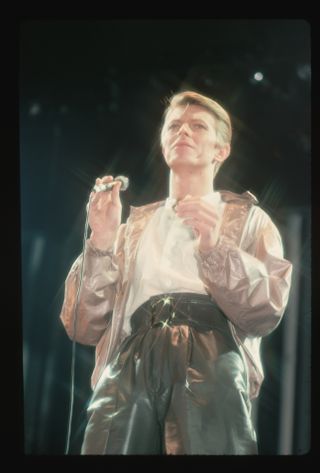 David Bowie, in brown leather pants, singing on stage.