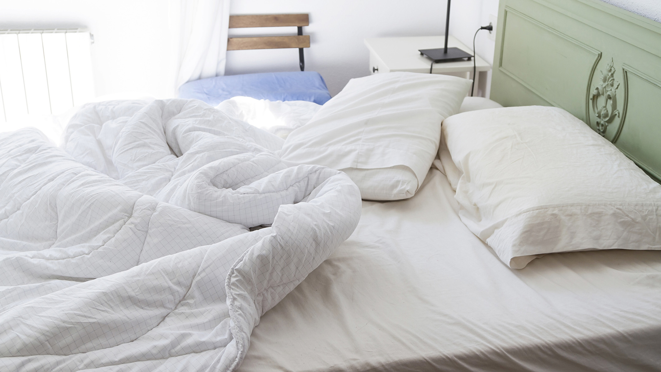 Image shows a white mattress with a green headboard covered in white bed linens and pillows