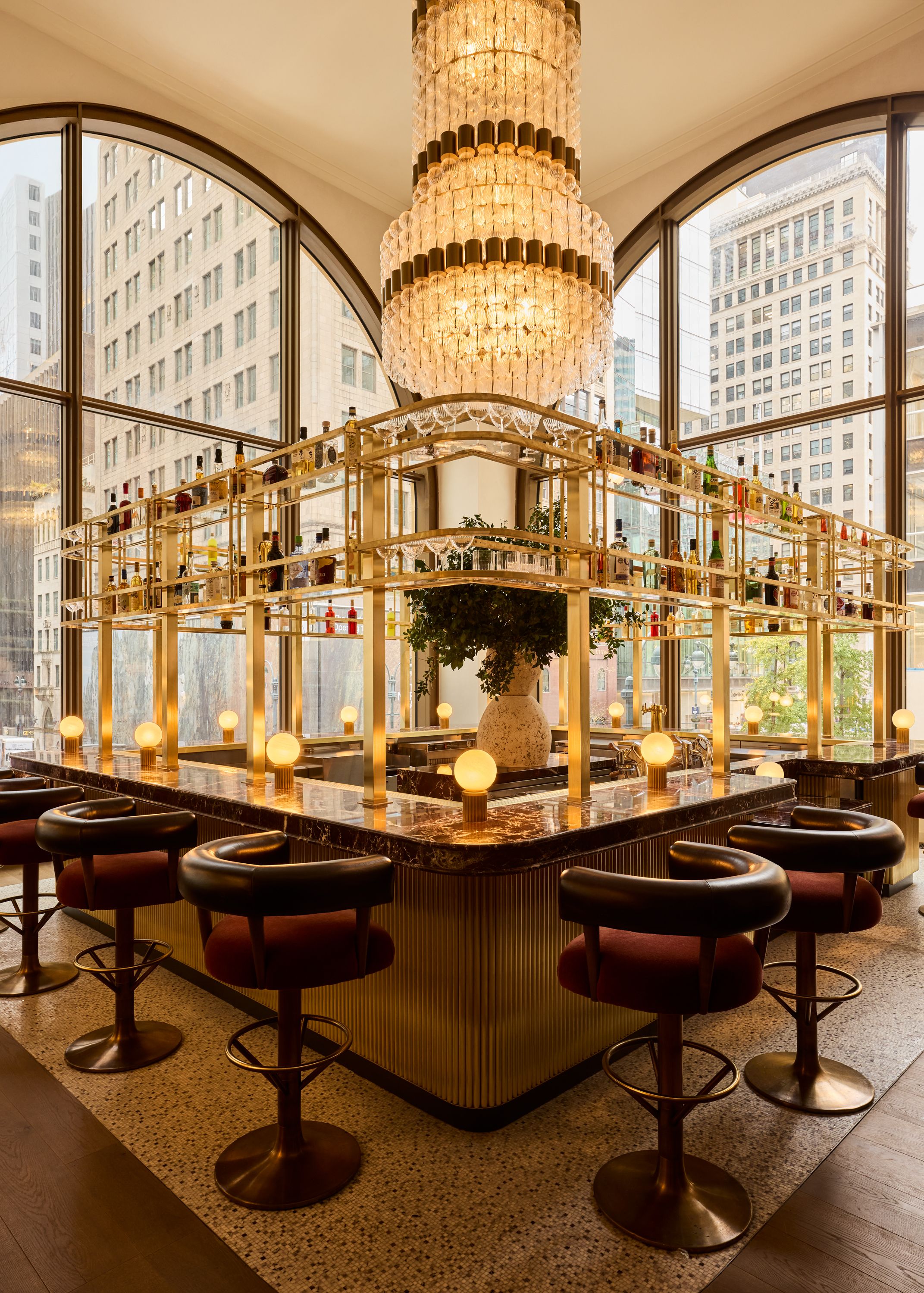 Image of a bar surrounded by stools in front of two large arched windows in a private club in NYC