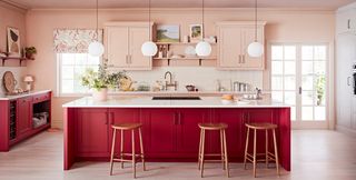 A red and pink kitchen with white worktops and wooden bar stools