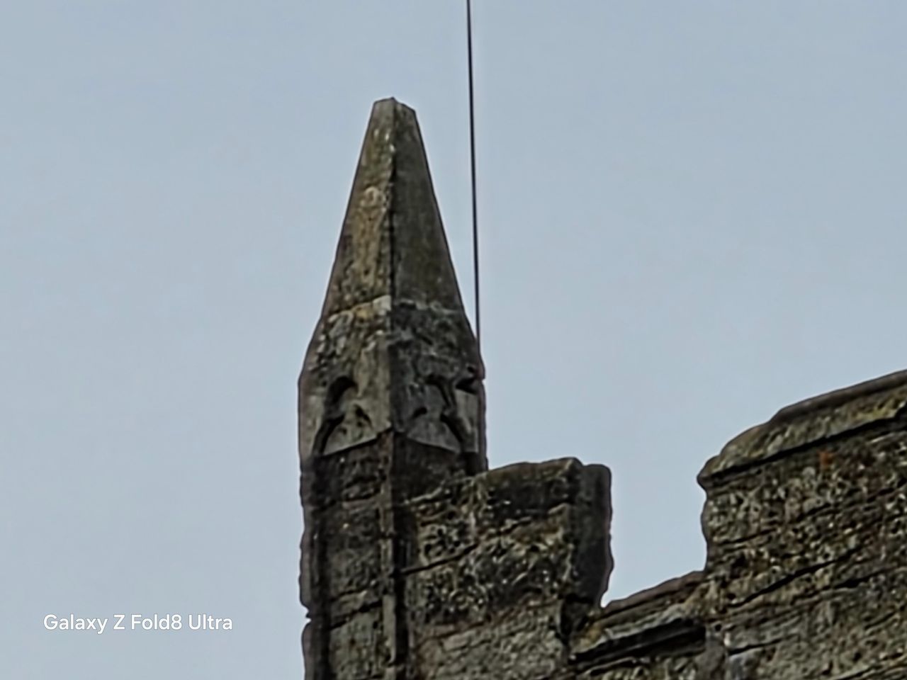 Extreme zoom view of a weathered pointed stone pinnacle on the corner of a church tower.