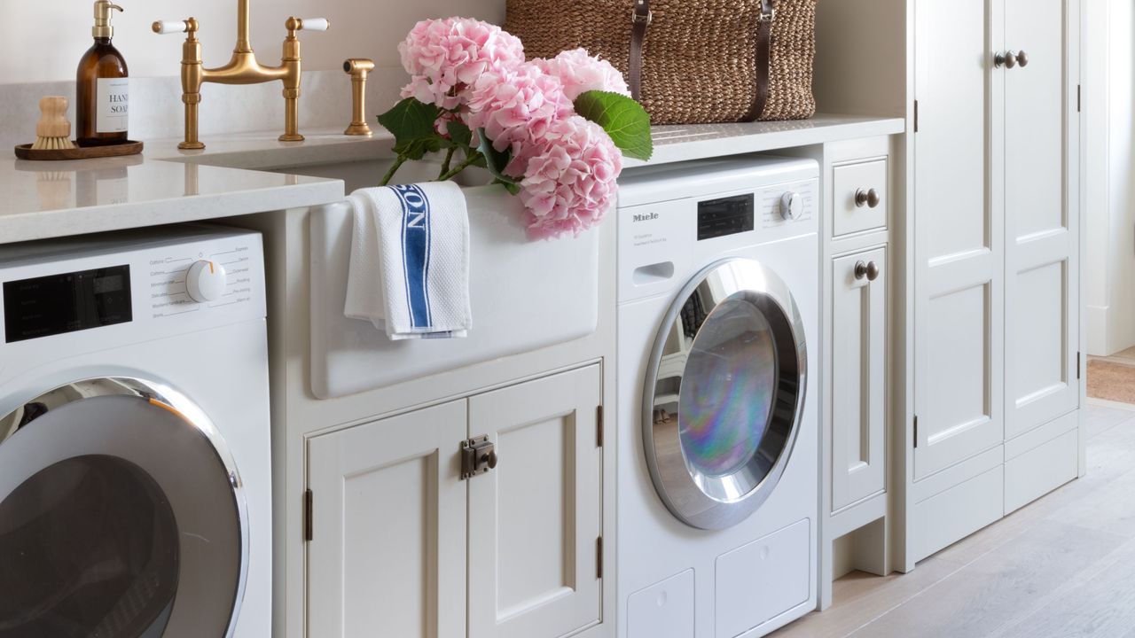 Utility room with integrated washing machine and tumble dryer and white cabinets