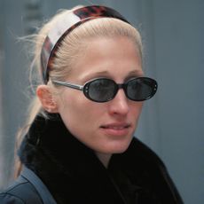 Carolyn Bessette Kennedy wears a brown headband and black oval sunglasses