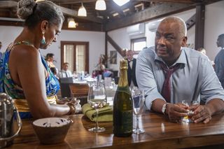 Jacqueline StClair (Cathy Tyson) stands at the bar in the Saint Marie Yacht Club, looking down nervously. Selwyn Patterson (Don Warrington) is leaning on the bar and looking at her with concern.