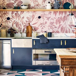 pink botanical wallpaper mural with wooden shelf and navy blue cabinetry with stainless steel appliances