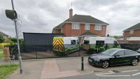 A large metal shed on a driveway with ambulances on a drive