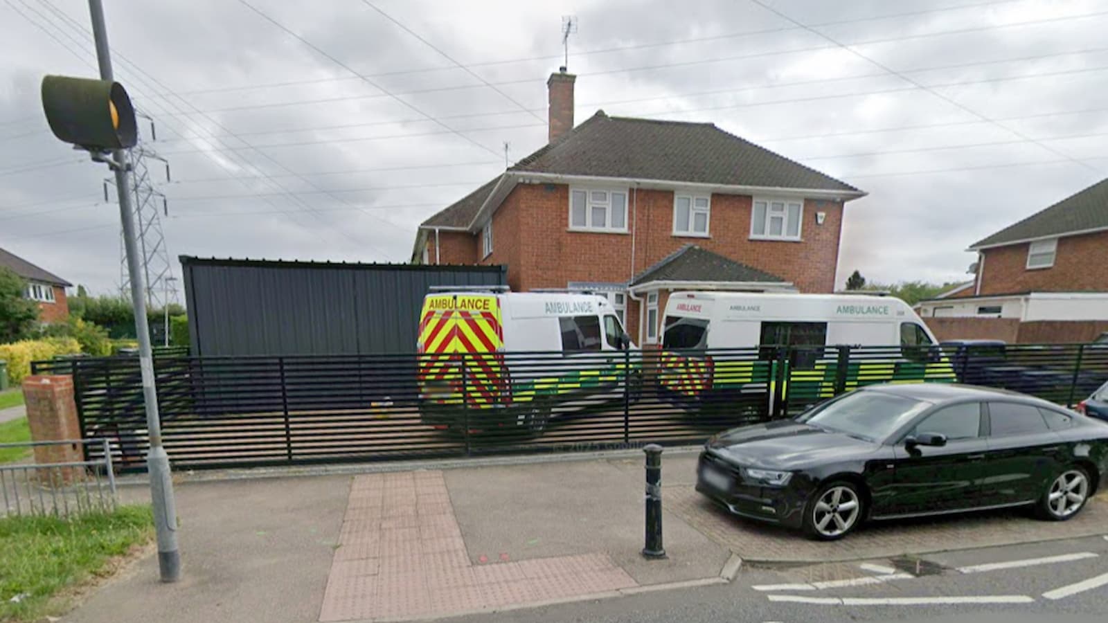A large metal shed on a driveway with ambulances on a drive