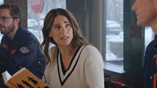 Lyndsy Fonseca holds a book and wears a sweater for The Bears' Chicago themed Hallmark movie 2026. 