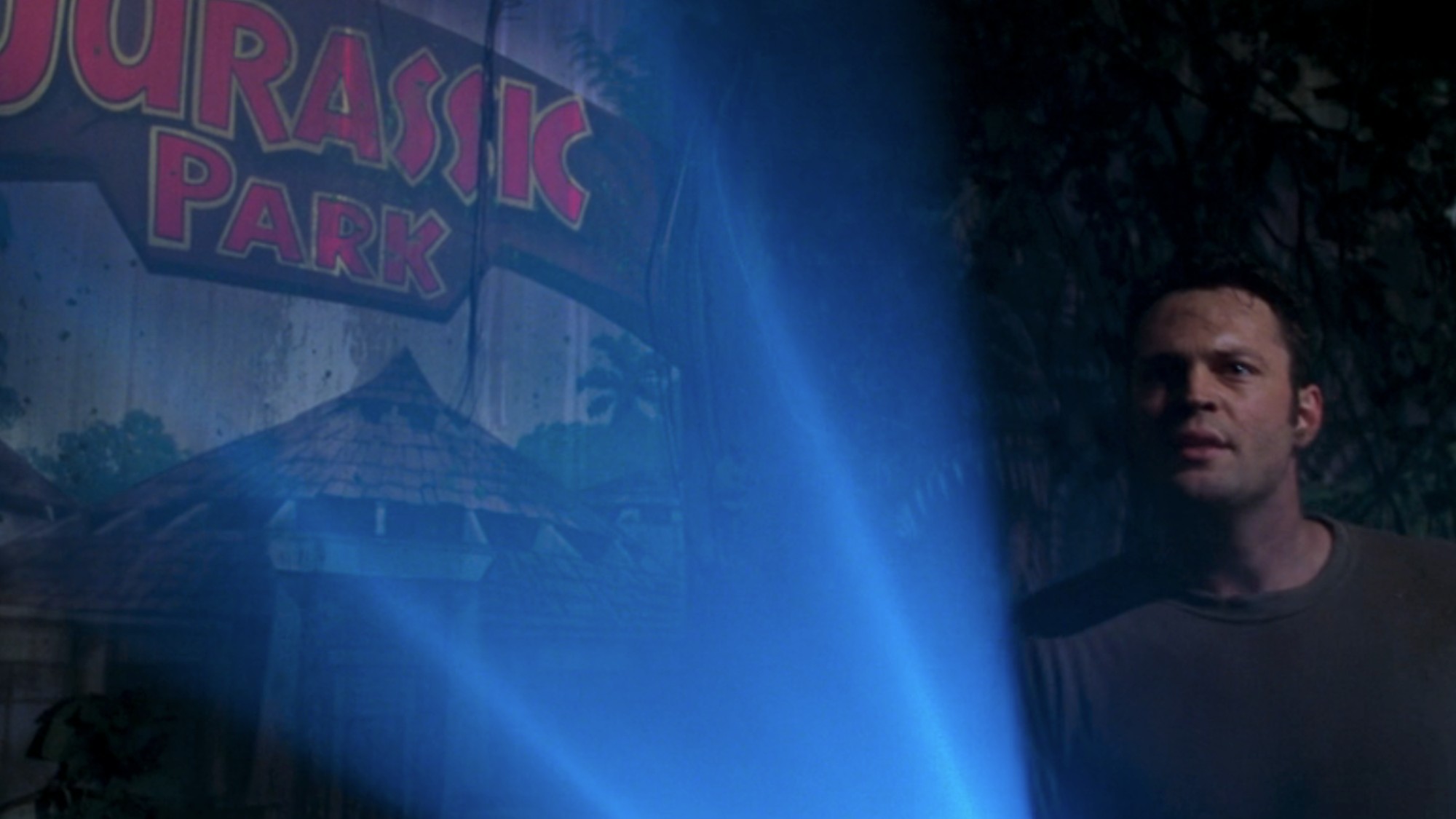 Vince Vaughn holding a flashlight in front of a Jurassic Park mural in The Lost World: Jurassic Park