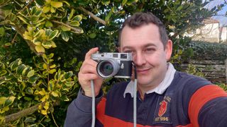 Leica M2 held in one had towards the photographers face who is smiling