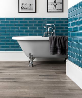 Teal wall tiles in bathroom with white bath and grey flooring by Flooring Mountain