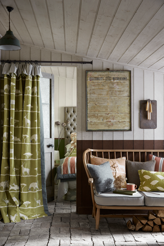 Vanessa Arbuthnot fabrics curtain ideas. Country living room with stone flooring, wooden paneled walls and ceiling, wooden spindled bench, green curtains.