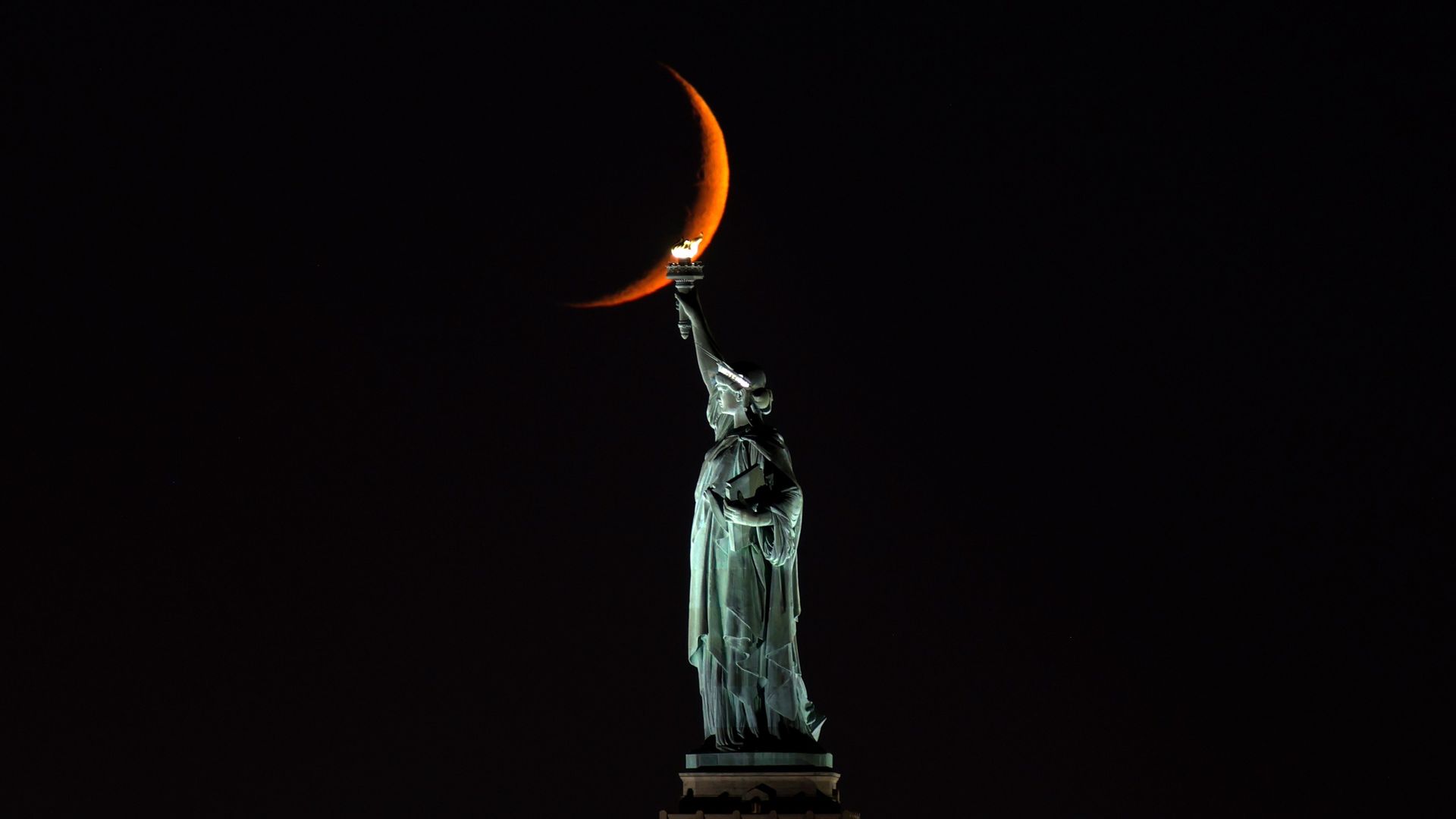 A ten percent illuminated waxing crescent moon sets behind the Statue of Liberty on October 13, 2026, in New York City.