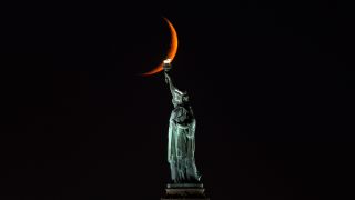 A ten percent illuminated waxing crescent moon sets behind the Statue of Liberty on October 13, 2026, in New York City. 