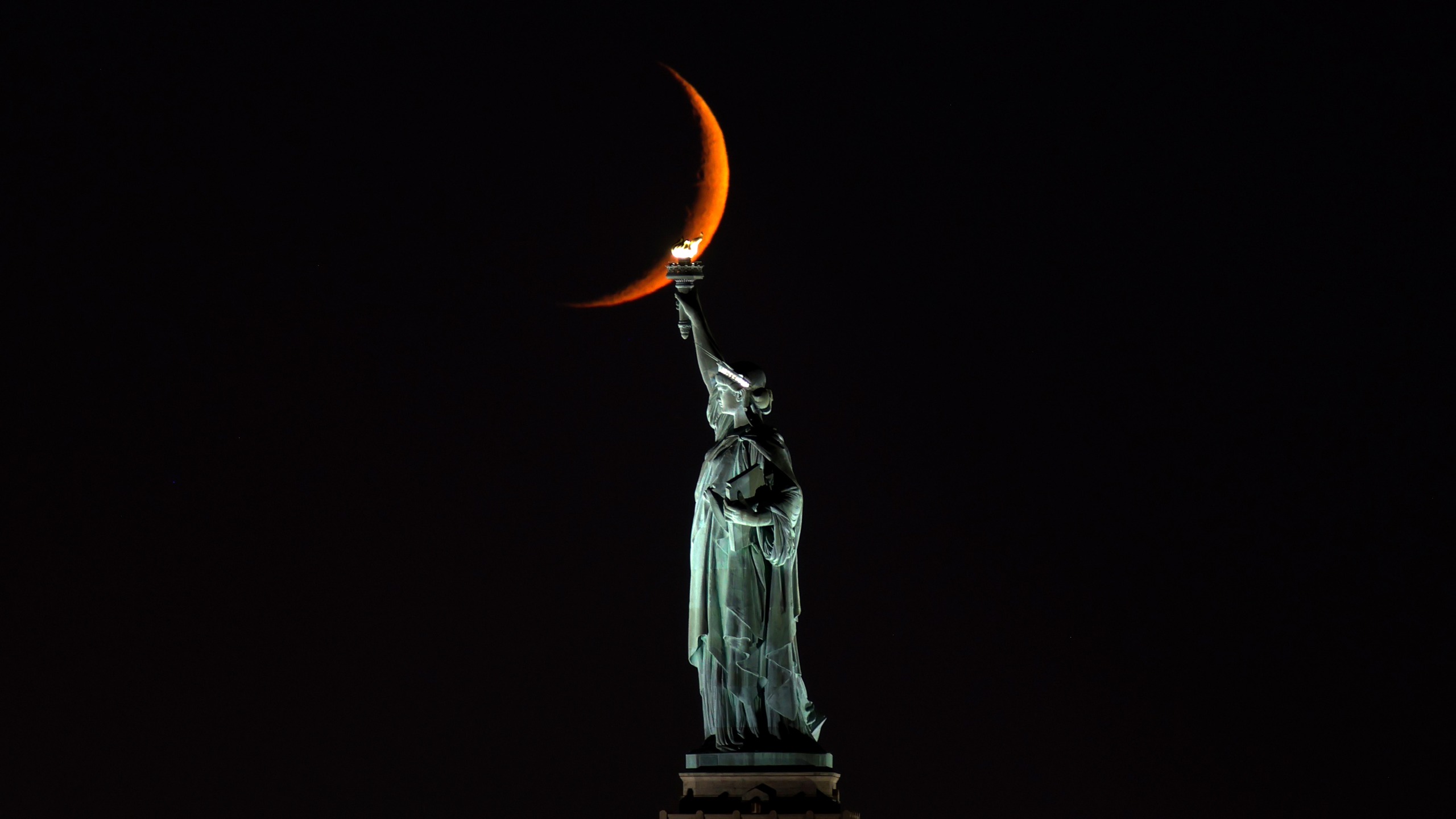 A ten percent illuminated waxing crescent moon sets behind the Statue of Liberty on October 13, 2026, in New York City. 