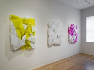 Three pieces of artwork consisting of crushed plastic in white and yellow, plain white, and white and pink