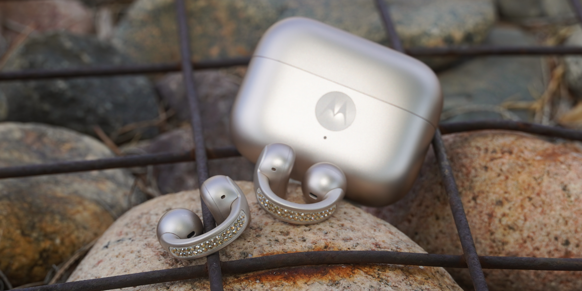 The Moto Buds Loop in PANTONE French Oak with Swarovski crystals on a rock beside their case.