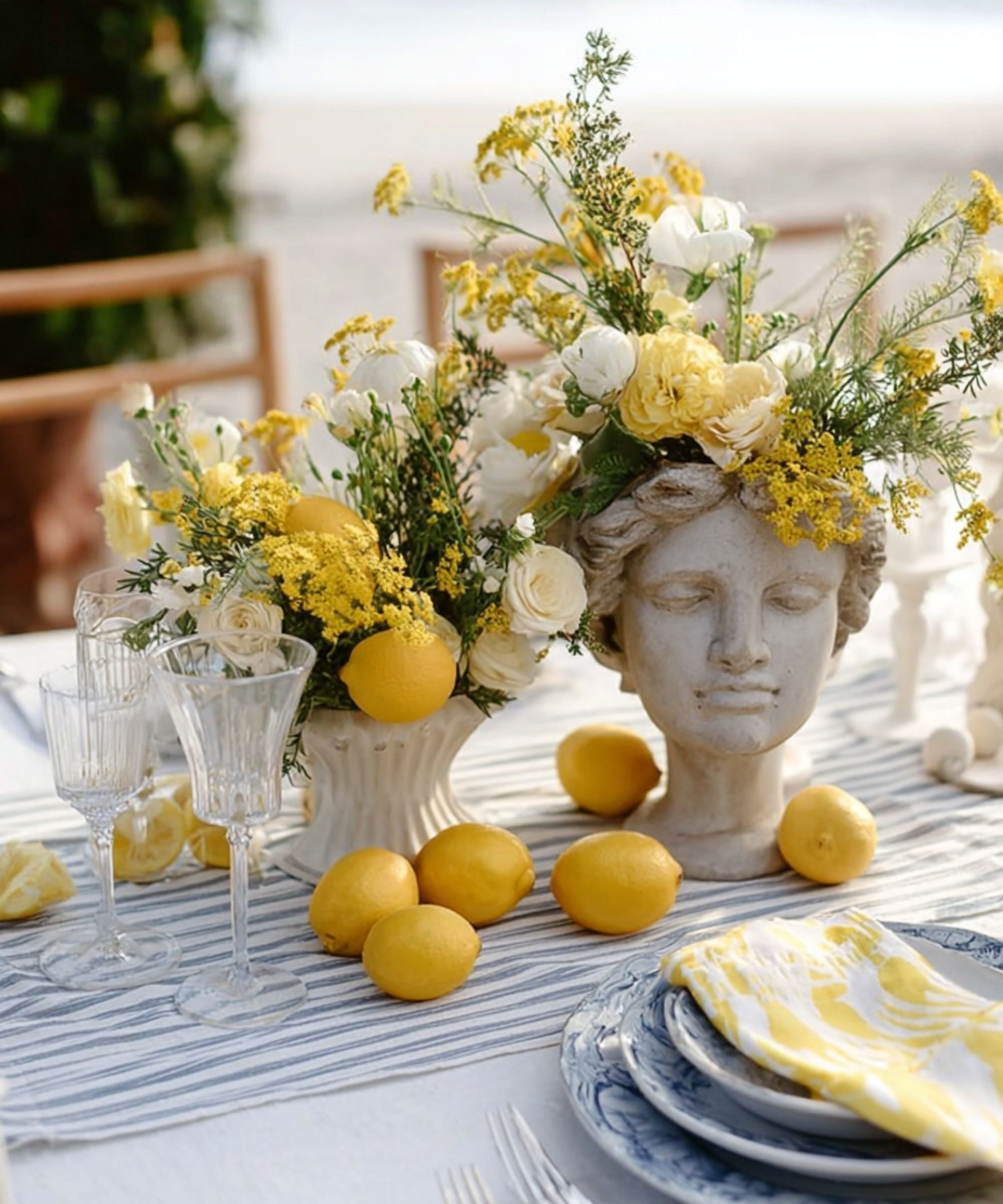 outdoor table decorated with lemons, yellow and white flowers and blue and white linens and plates