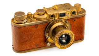 Vintage brass camera with leather casing, featuring various knobs and a prominent Elmar lens, showcasing classic photography design.