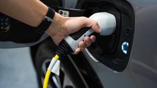 A human hand holds a charger to an electric car charging point
