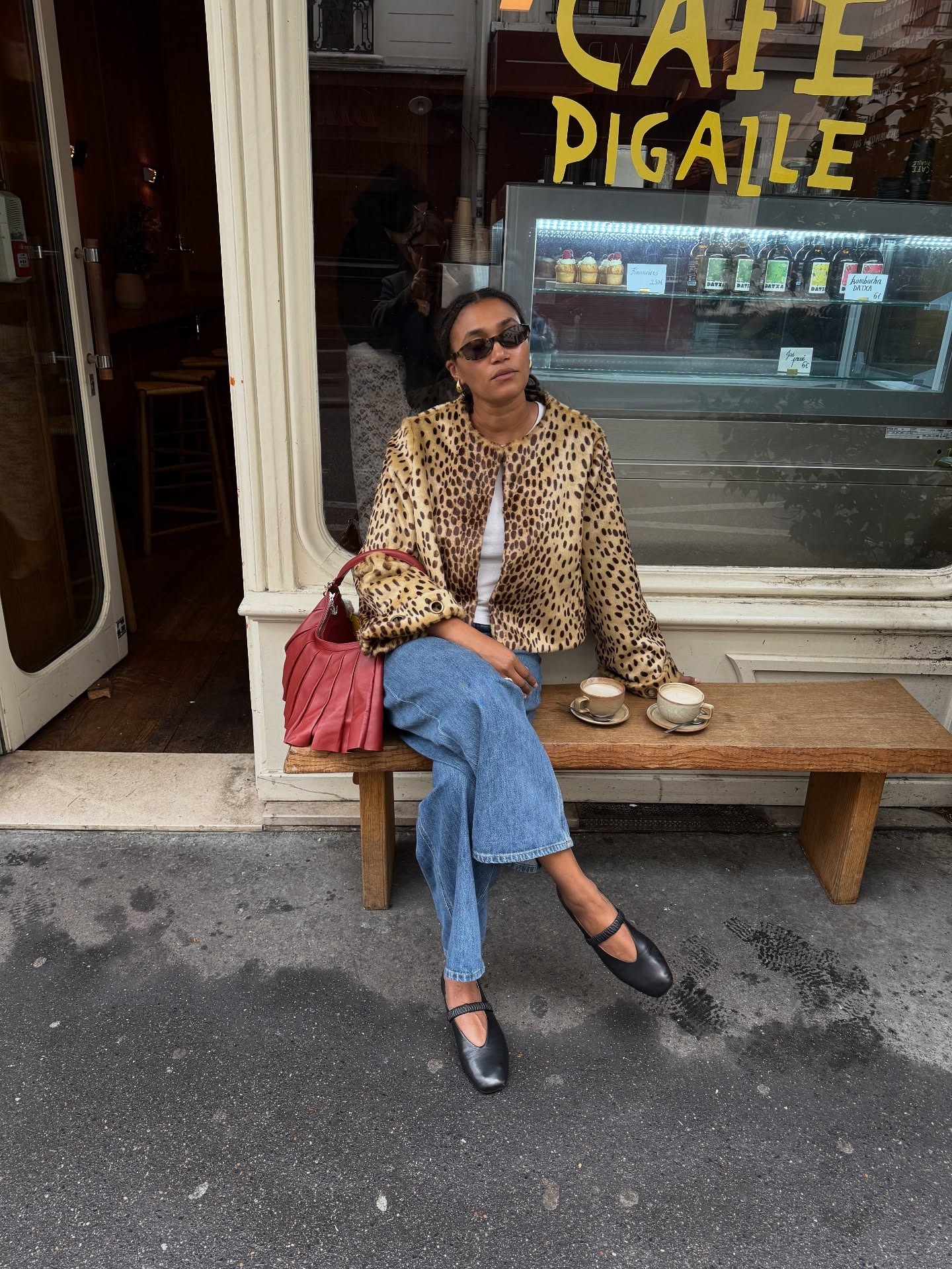 Influencer @lenafarl sits outside on a bench wearing a leopard print cropped jacket, blue jeans and ballet flats